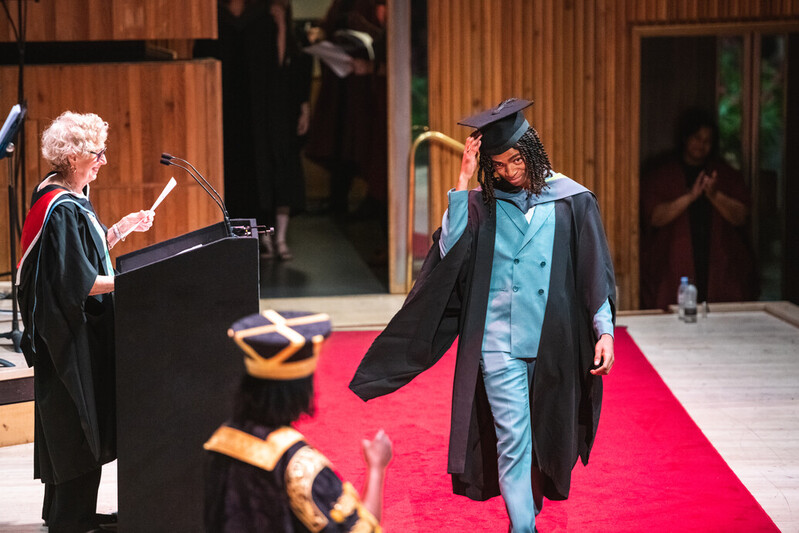 A UCA graduate tips his cap to the ceremonial procession in a bright blue suit