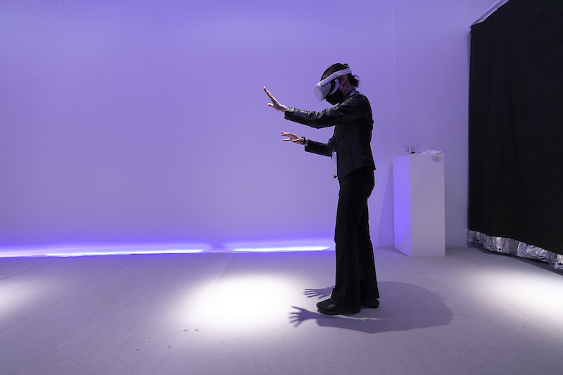 A person stands in a purple lit room with a VR headset on