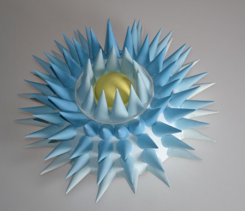 An image showing a ceramic wall sculpture of a representation of a pollen spore, coloured blue with a yellow centre
