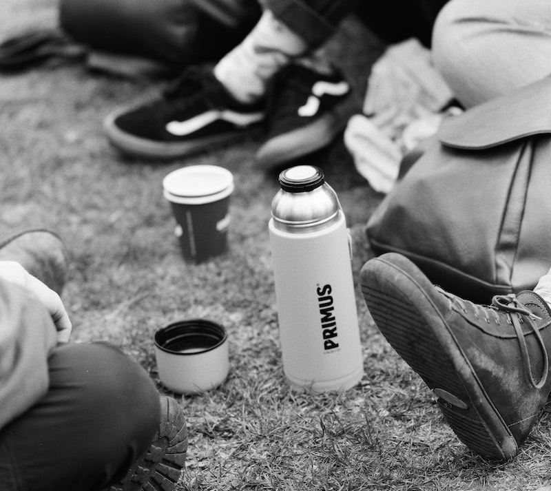 Black and white photo shows several people sitting - just out of shot - around a large flask with a hot drink. Image by Benjamin Kaufmann via Unsplash