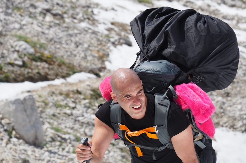Image shows Paul Robinson climbing a mountain in the Dolomites, carrying a backpack and his pink bear suit